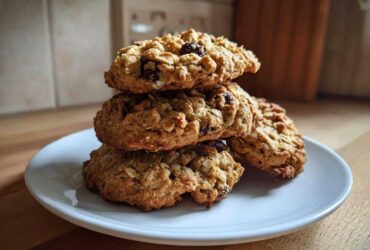 A stack of four golden brown oatmeal cookies, visible raisins, resting on a white plate.