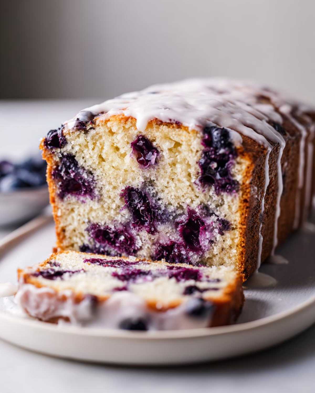A close-up of a sliced blueberry breakfast cake loaf topped with white vanilla glaze.