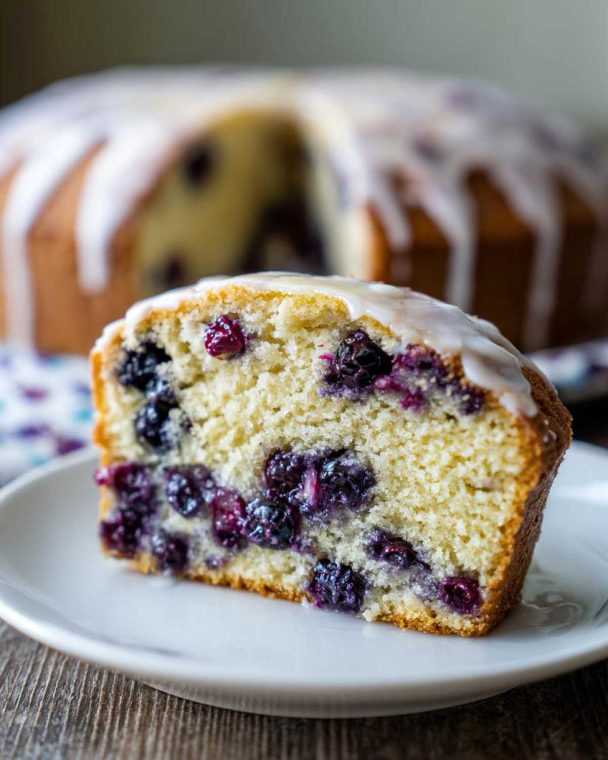 Close-up of a slice of moist blueberry breakfast cake topped with white vanilla glaze.
