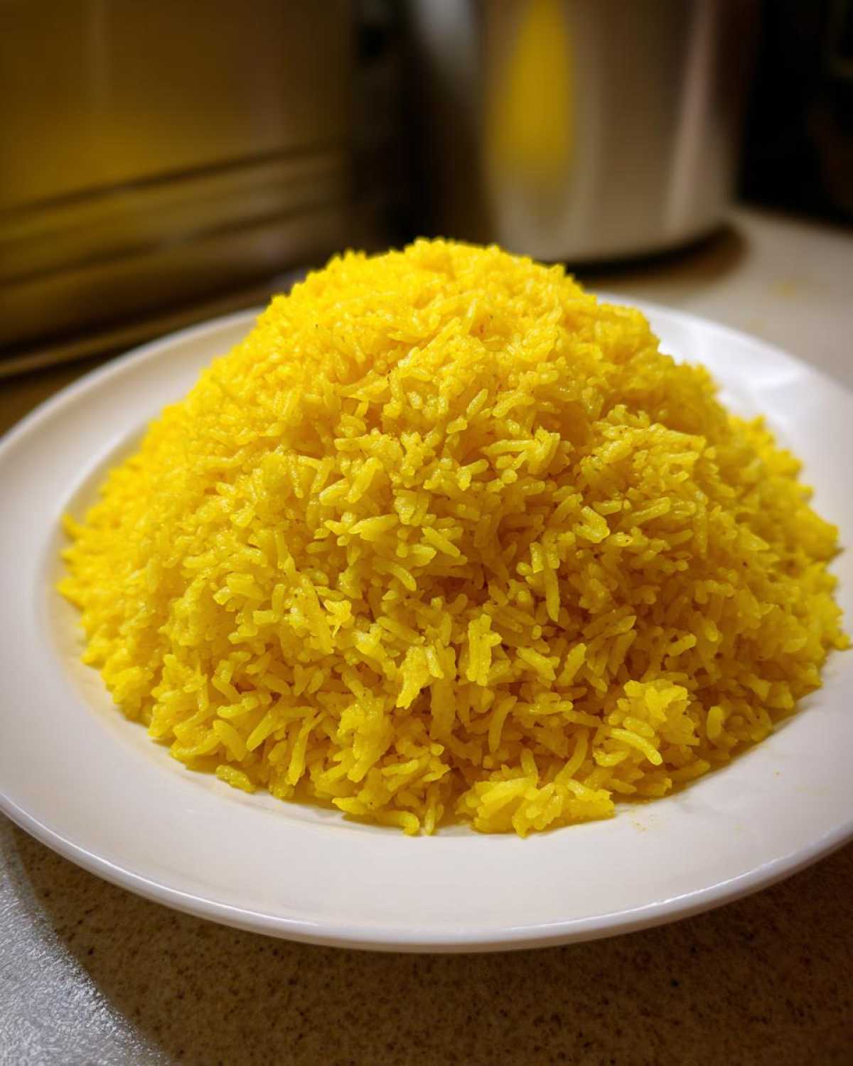 A close-up shot of a large, perfectly mounded serving of bright yellow turmeric rice on a white plate.