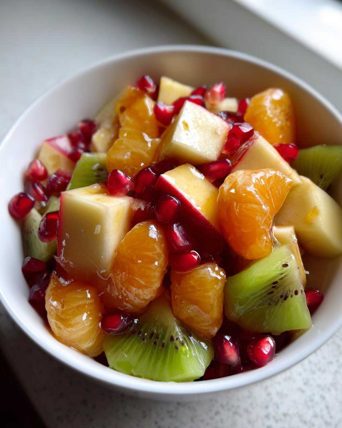 Close-up of a bright winter fruit salad featuring kiwi, orange segments, apple chunks, and pomegranate seeds.