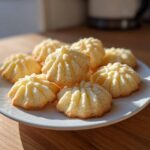 A plate piled high with freshly baked, ridged butter cookie treats, highlighted by natural sunlight.
