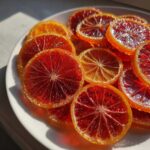Close-up of glistening, jewel-toned candied orange slices, featuring deep red blood oranges and lighter orange slices.