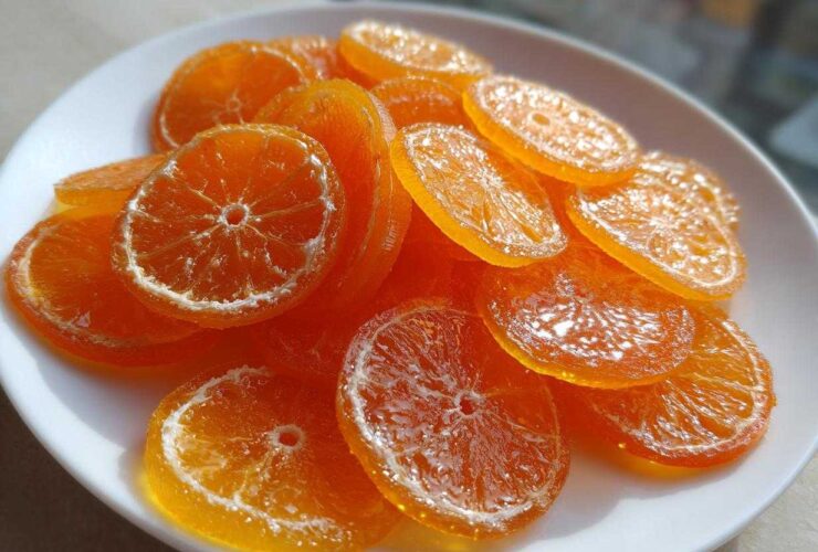 A white plate piled high with glistening, translucent candied orange slices, showcasing their vibrant color.