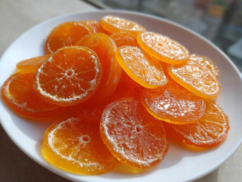 A white plate piled high with glistening, translucent candied orange slices, showcasing their vibrant color.