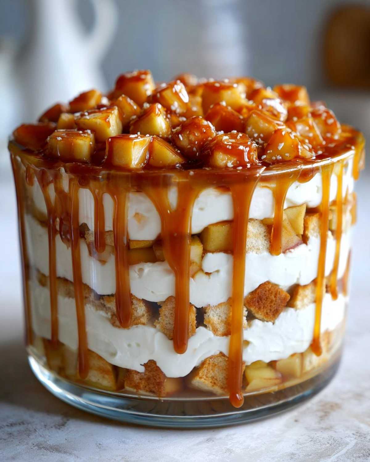 Close-up of a layered caramel apple trifle featuring cake pieces, cream, and heavy caramel drizzle.