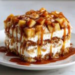 A decadent slice of caramel apple trifle showing layers of cake, cream, and topped with caramelized apples and thick caramel sauce.
