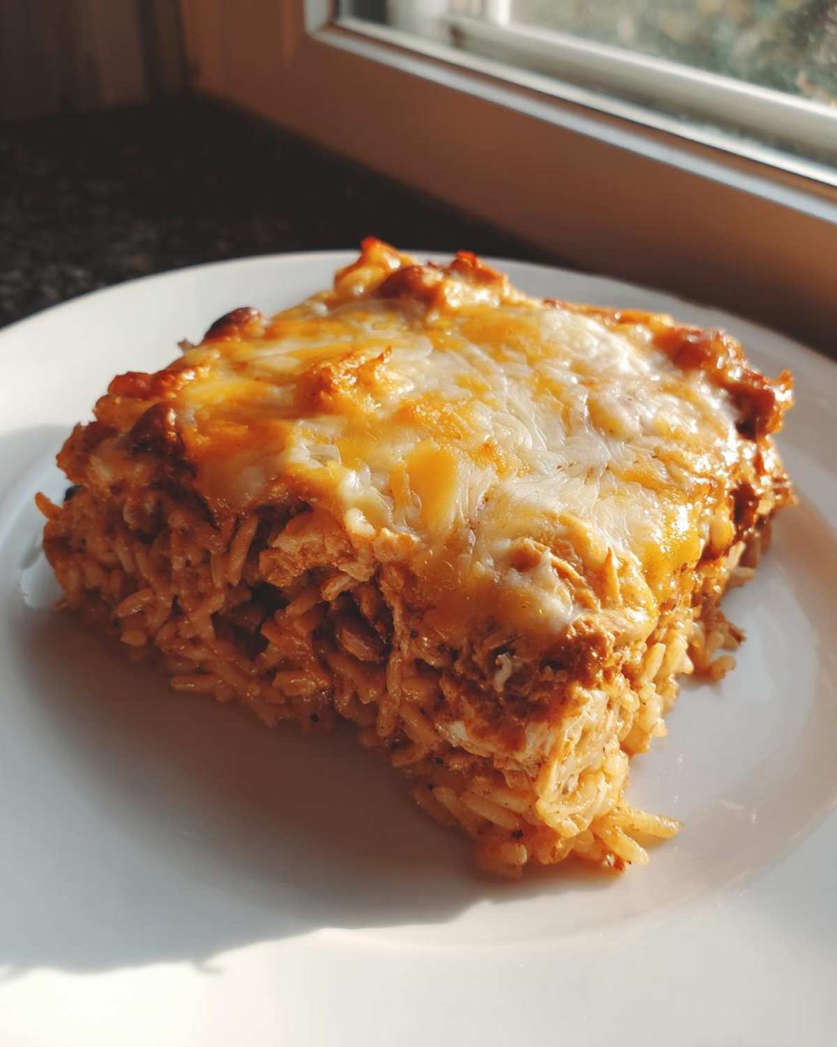 A close-up slice of cheesy, baked burrito bake featuring rice and seasoned filling, served on a white plate.