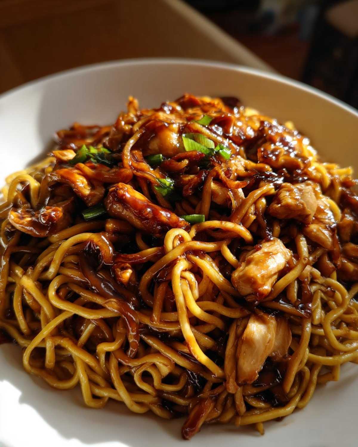 A close-up view of glossy noodles and chunks of chicken coated in dark sauce, part of the chicken chow mein recipe.
