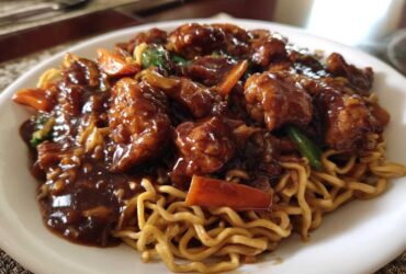 Close-up of a white plate featuring saucy chicken pieces and vegetables served over egg noodles in a chicken chow mein recipe.
