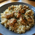 Close-up of pan-seared chicken pieces served over creamy garlic parmesan rice, garnished with parsley.