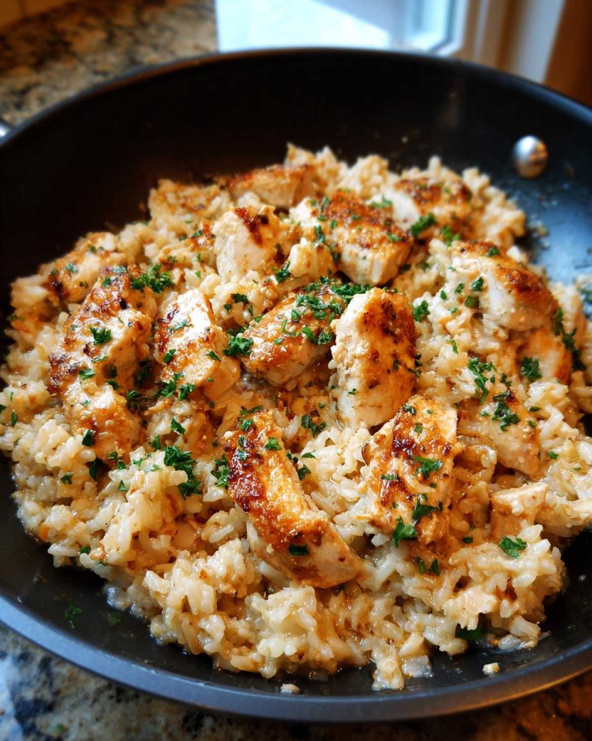 Close-up of chicken scampi with garlic parmesan rice, topped with fresh parsley, served in a black skillet.