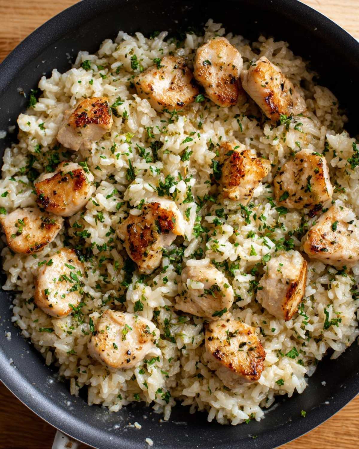 Close-up overhead view of pan-seared chicken pieces mixed with garlic parmesan rice and fresh parsley.