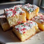 Stack of square-cut christmas gooey butter cookies topped with powdered sugar and red and green sprinkles.
