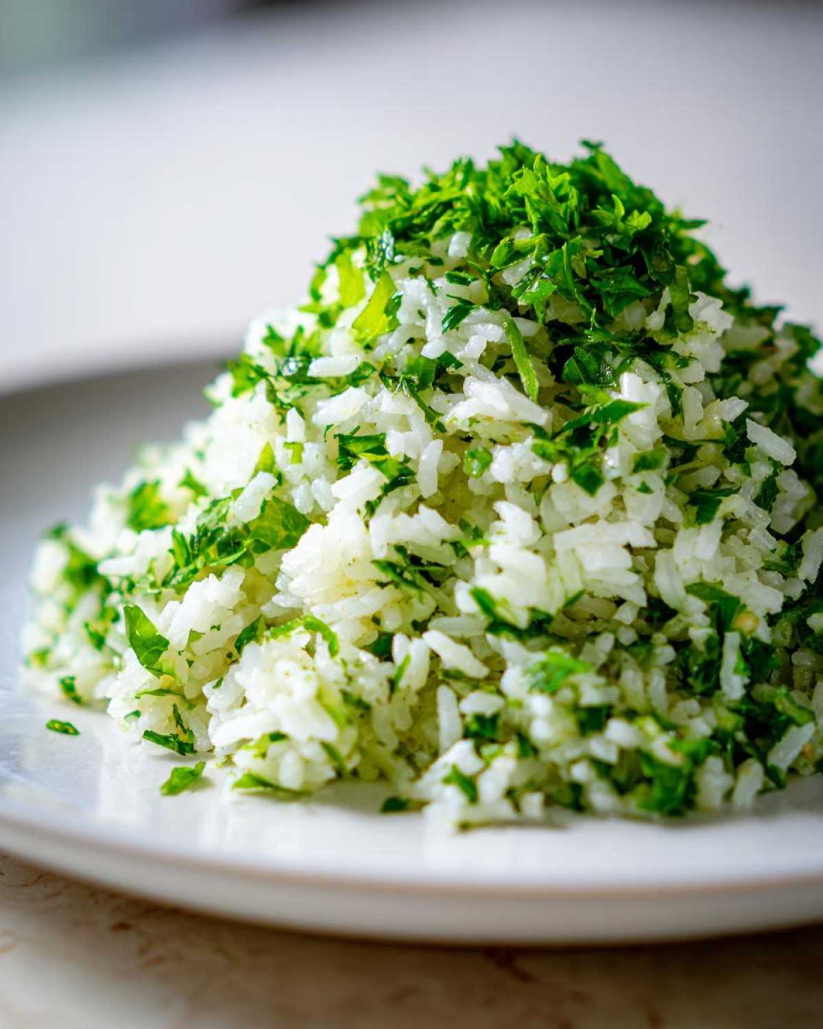 A close-up of fluffy cilantro lime rice piled high on a white plate, topped generously with chopped fresh cilantro.