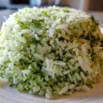 A close-up of fluffy white rice mixed with bright green cilantro lime rice seasoning, molded into a dome shape.