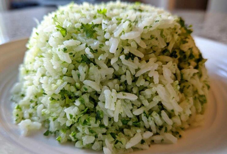 A close-up of fluffy white rice mixed with bright green cilantro lime rice seasoning, molded into a dome shape.