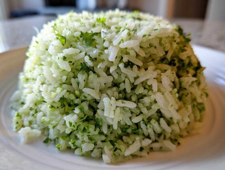 A close-up of fluffy white rice mixed with bright green cilantro lime rice seasoning, molded into a dome shape.