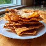 A tall stack of crispy, golden-brown buñuelos dusted heavily with cinnamon sugar, served on a white plate.
