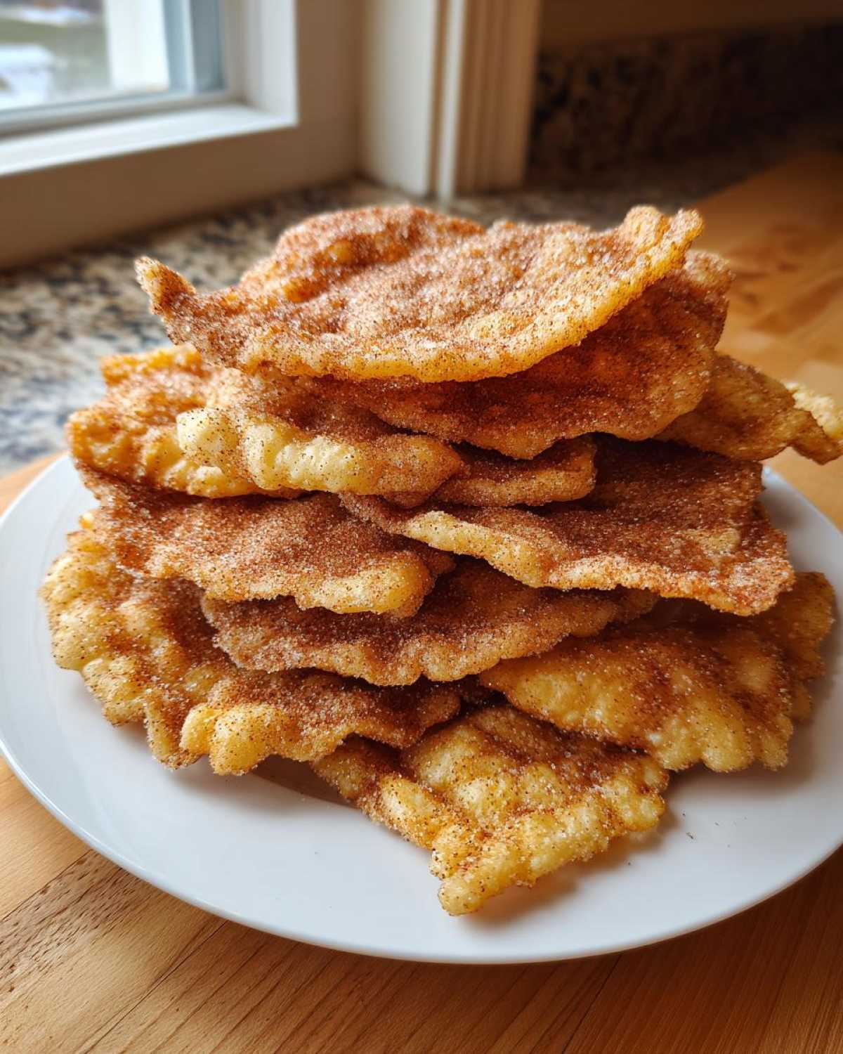 A tall stack of freshly fried buñuelos generously coated in cinnamon sugar, resting on a white plate.