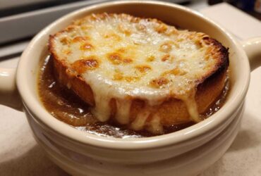 Close-up of a bowl of rich french onion soup recipe topped with a thick, broiled cheese crust on bread.