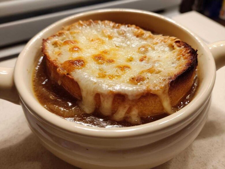 Close-up of a bowl of rich french onion soup recipe topped with a thick, broiled cheese crust on bread.
