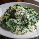 Close-up of a generous serving of rich creamed spinach recipe topped with red pepper flakes in a white bowl.