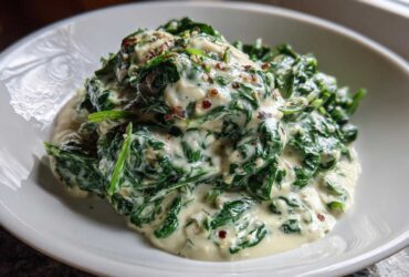 Close-up of a generous serving of rich creamed spinach recipe topped with red pepper flakes in a white bowl.