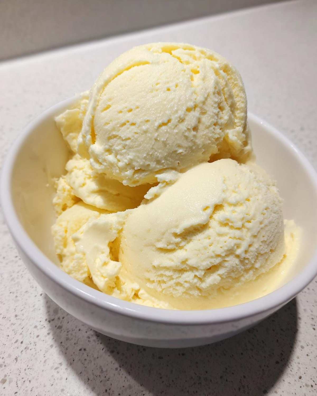 Close-up of three scoops of creamy, pale yellow banana ice cream served in a small white bowl.