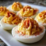 Close-up of creamy deviled eggs piped high and dusted with paprika on a white platter.