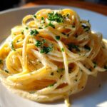 Close-up of creamy spaghetti tossed in a rich sauce, topped with fresh parsley, representing a garlic parmesan dish.