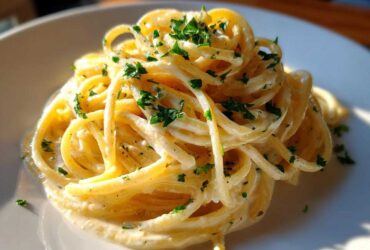 Close-up of creamy spaghetti tossed in a rich sauce, topped with fresh parsley, representing a garlic parmesan dish.