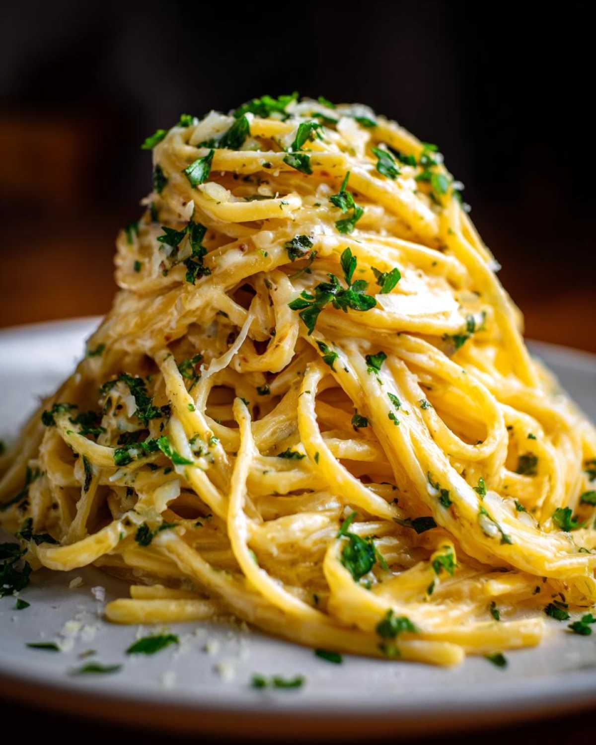 A tall mound of creamy spaghetti coated in a rich garlic parmesan sauce and topped with fresh parsley.