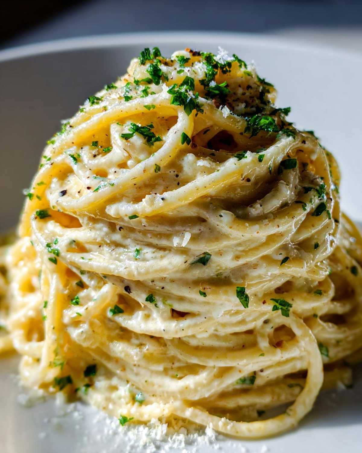 A tall twirl of creamy pasta coated in a rich sauce, topped with fresh parsley and grated garlic parmesan cheese.