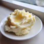 A dollop of fluffy, creamy mashed potatoes topped with a pool of melted butter, served on a small white plate.