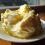 A generous scoop of light yellow, fluffy creamy mashed potatoes served on a small white plate.