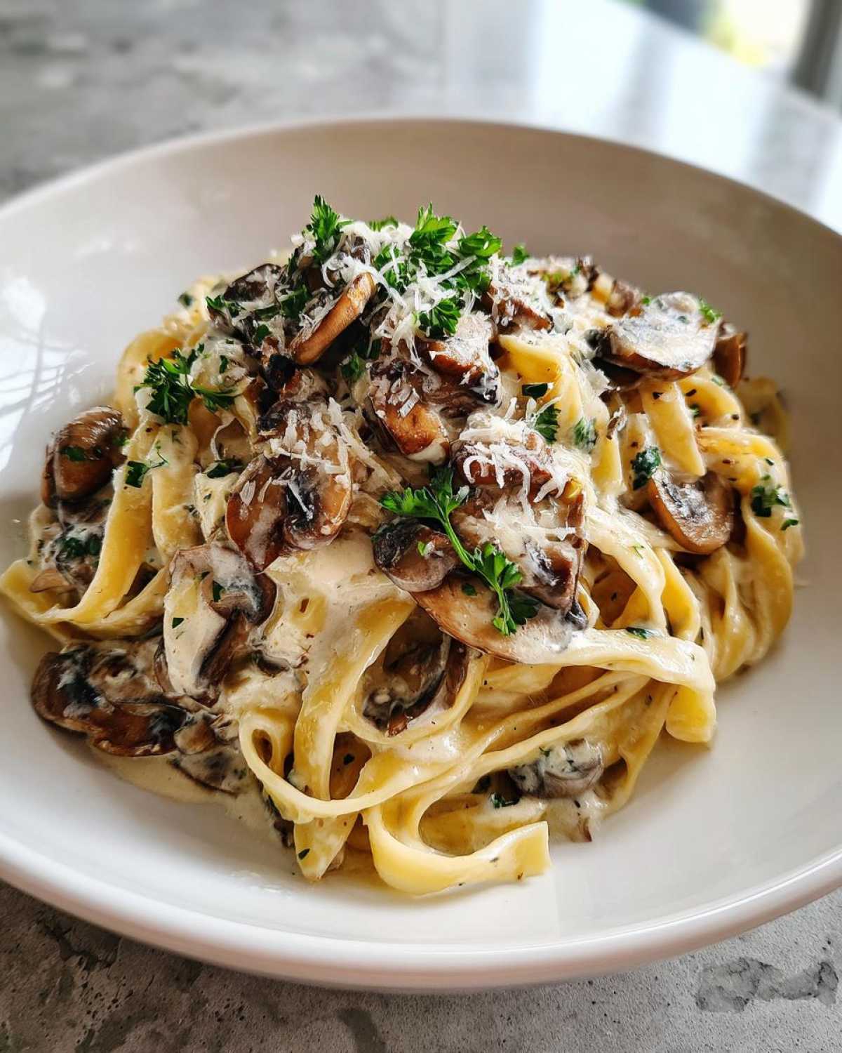 Close-up of creamy fettuccine mushroom pasta topped with grated parmesan and fresh parsley.