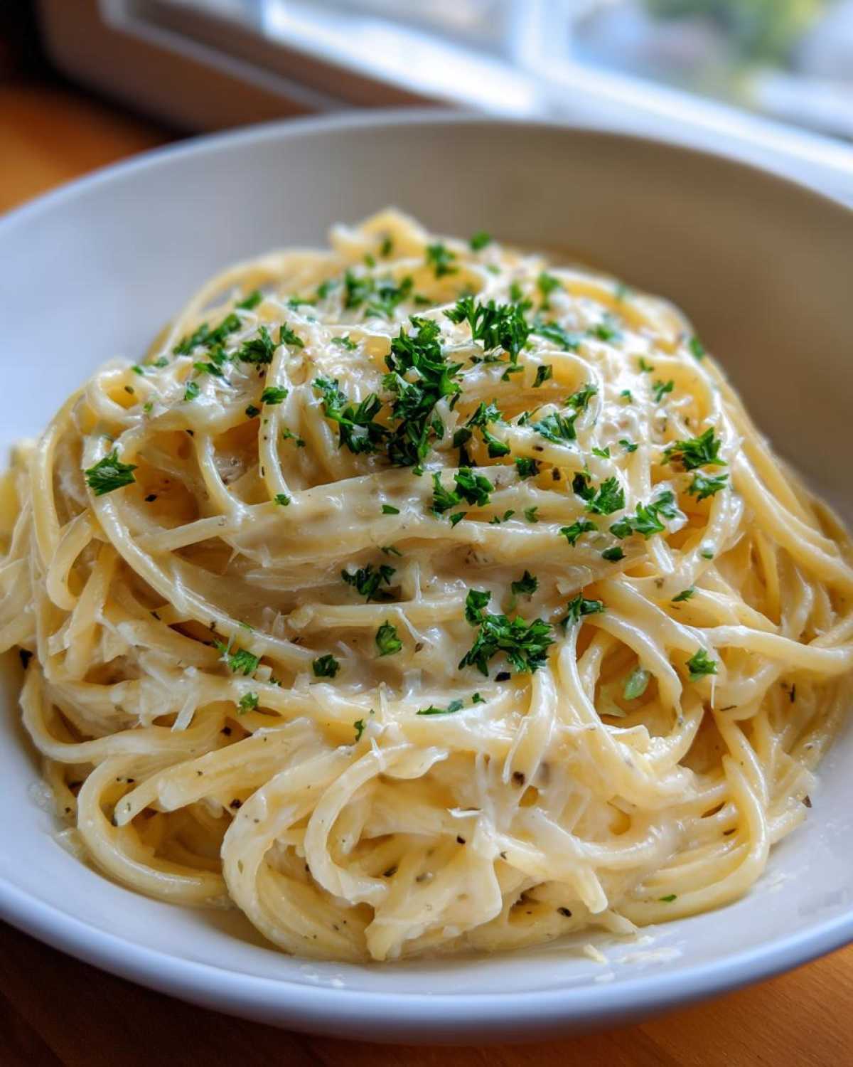 Close-up of creamy parmesan pasta coated in sauce and topped with fresh chopped parsley in a white bowl.