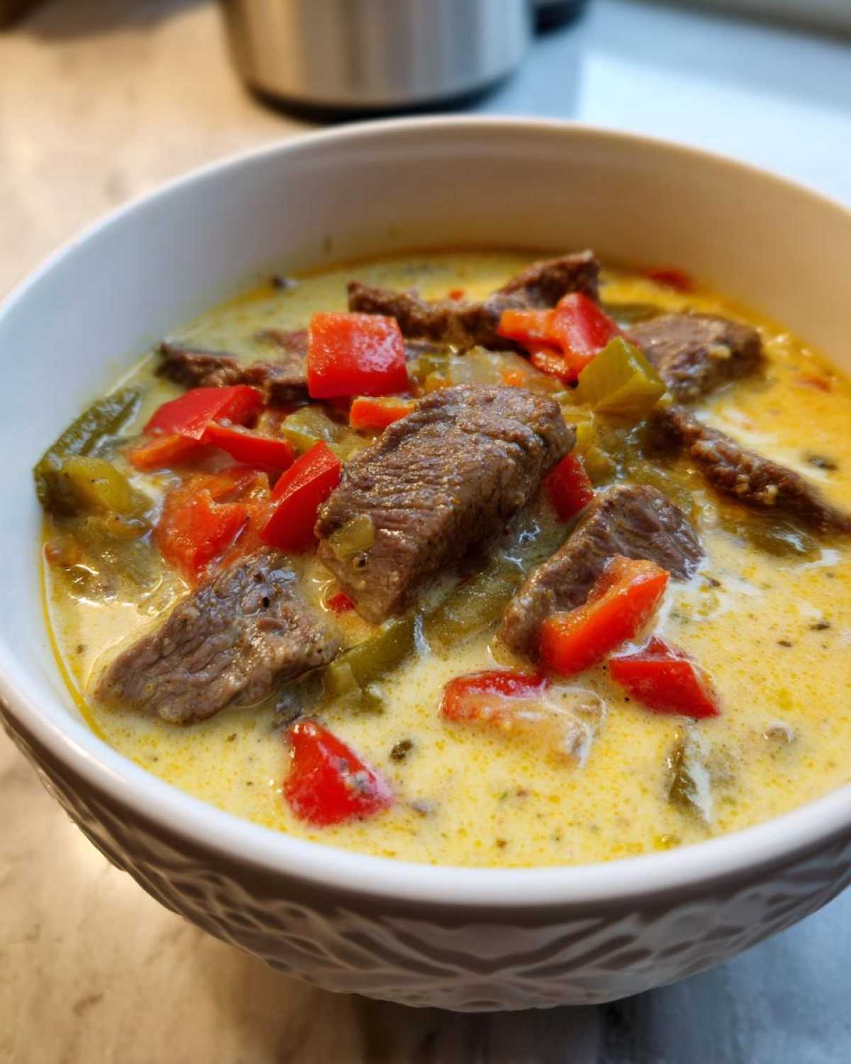Close-up of a bowl of creamy philly cheese steak soup featuring slices of steak, red peppers, and green peppers.