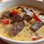 Close-up of a bowl of creamy philly cheese steak soup featuring chunks of steak, red and yellow peppers, and onions.