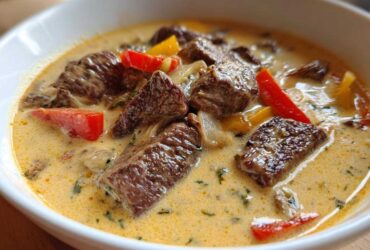 Close-up of a bowl of creamy philly cheese steak soup featuring chunks of steak, red and yellow peppers, and onions.