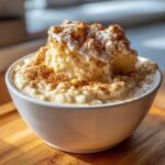A close-up of a creamy bowl of rice pudding topped with whipped cream and a generous dusting of cinnamon.