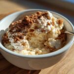 A close-up of creamy rice pudding topped with whipped cream and a generous dusting of cinnamon.