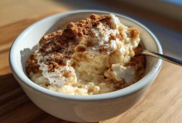 A close-up of creamy rice pudding topped with whipped cream and a generous dusting of cinnamon.