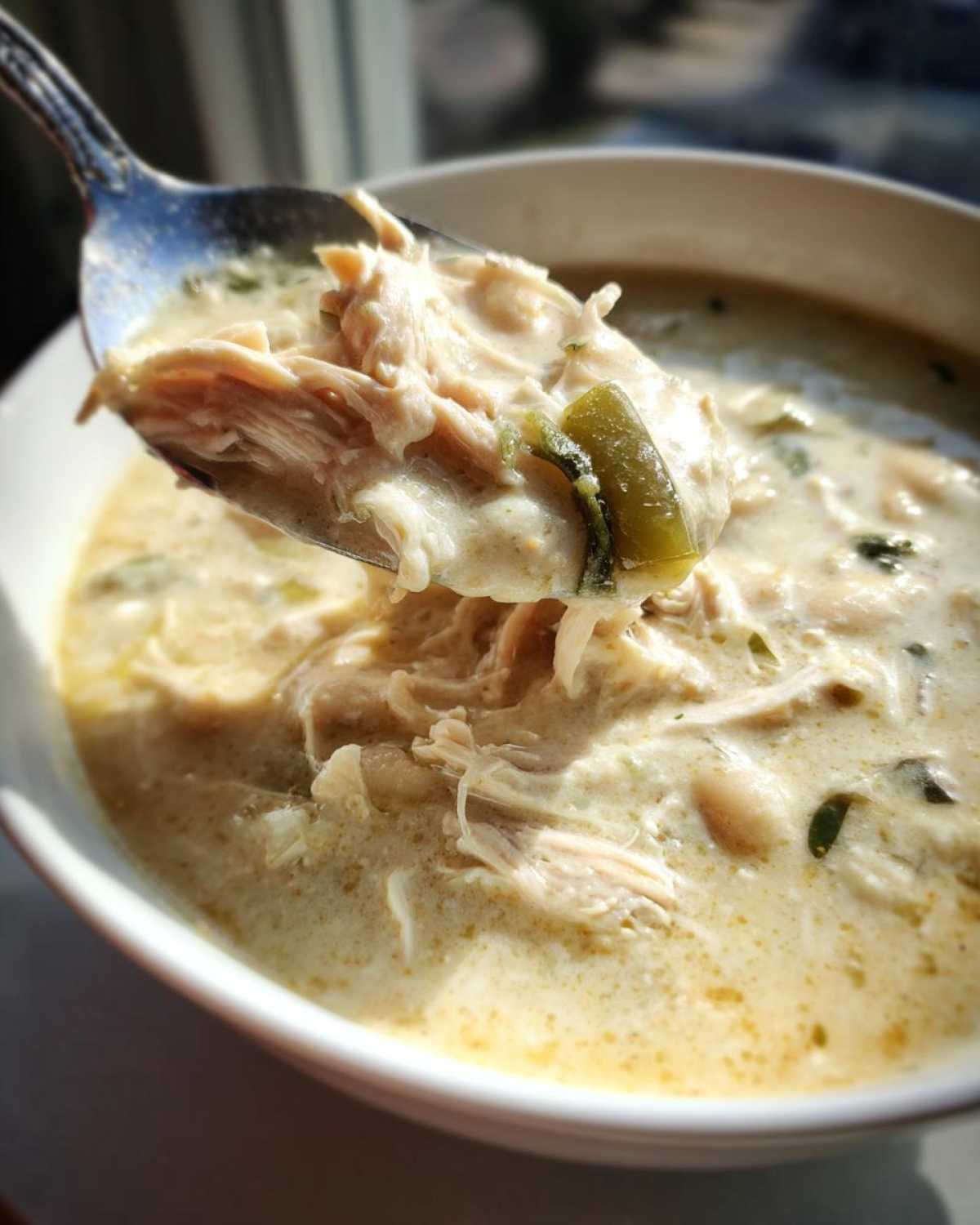 A spoonful of creamy white chicken chili, featuring shredded white chicken and green chilies, lifted from a bowl.