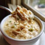 A spoonful of creamy white chicken chili, rich with shredded white chicken and beans, lifted from a white bowl.