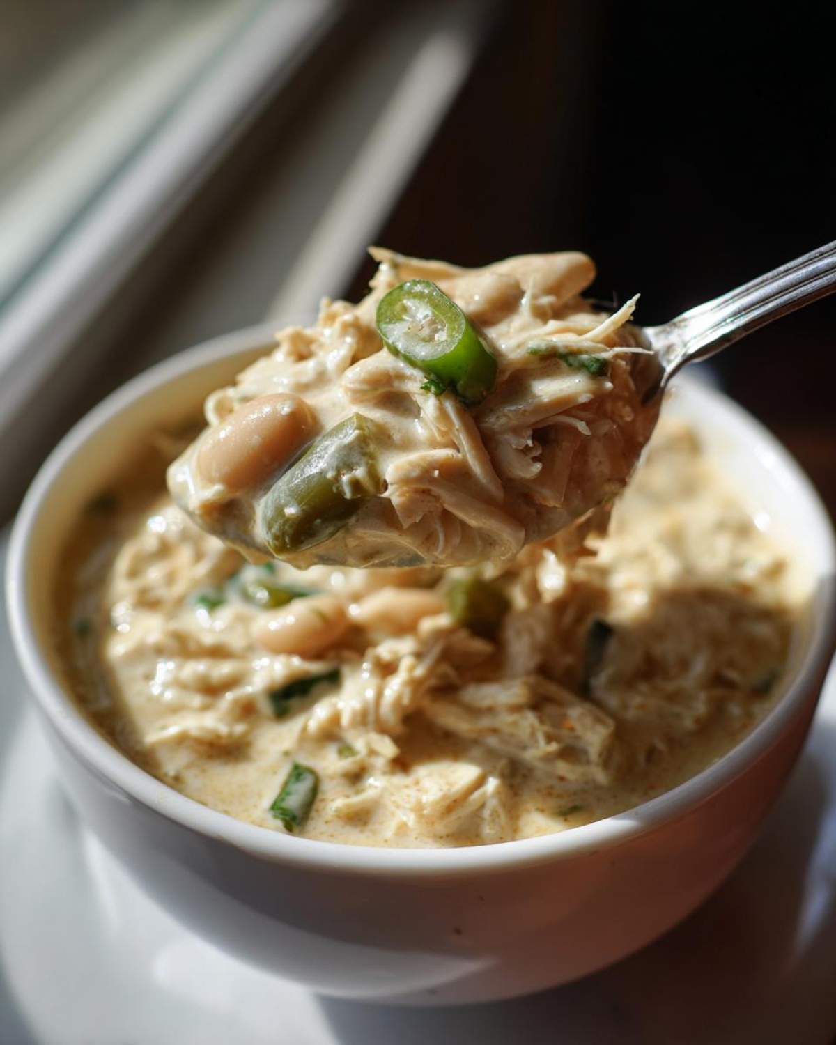 A spoonful of creamy white chicken chili, rich with shredded white chicken, beans, and topped with a slice of jalapeño.