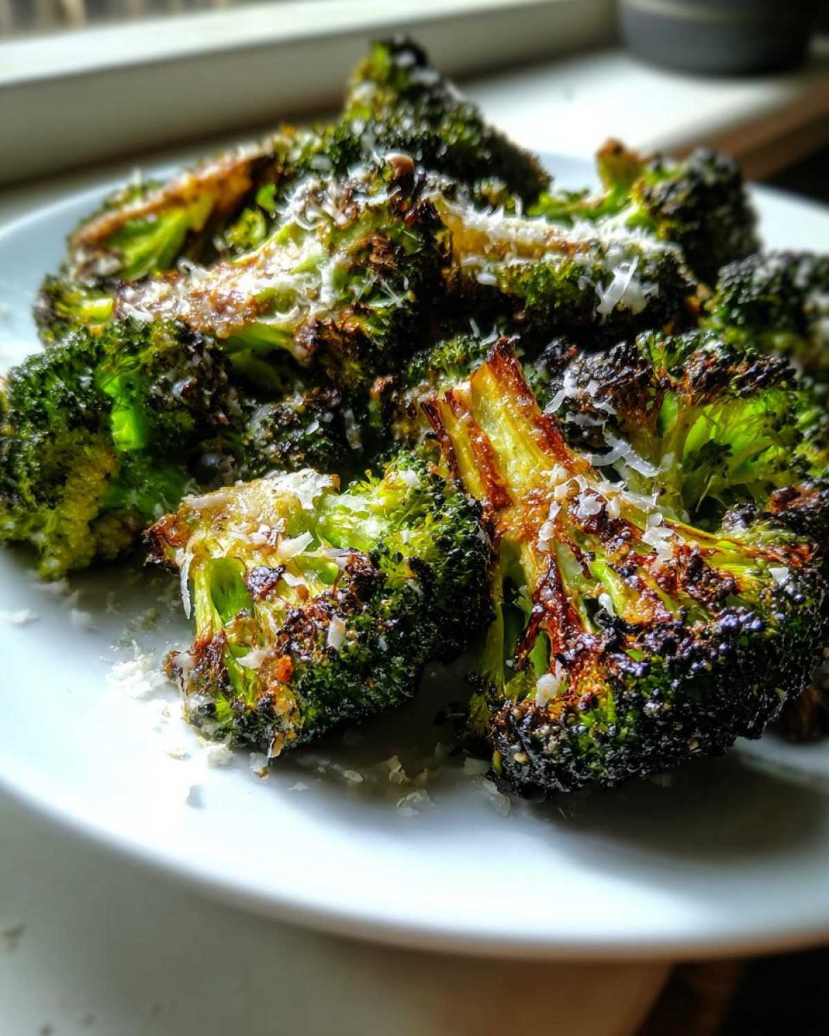 Close-up of perfectly crisp roasted broccoli florets topped with grated Parmesan cheese.