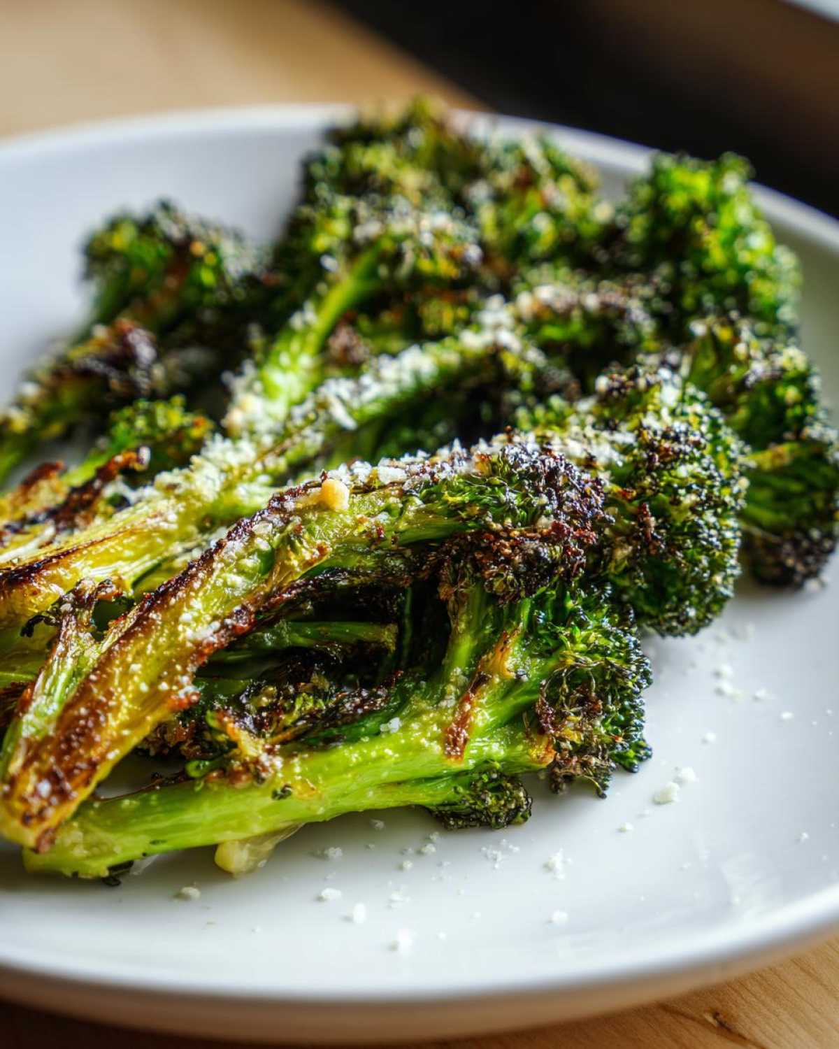 Close-up of crispy, charred roasted broccoli florets topped with grated Parmesan cheese.