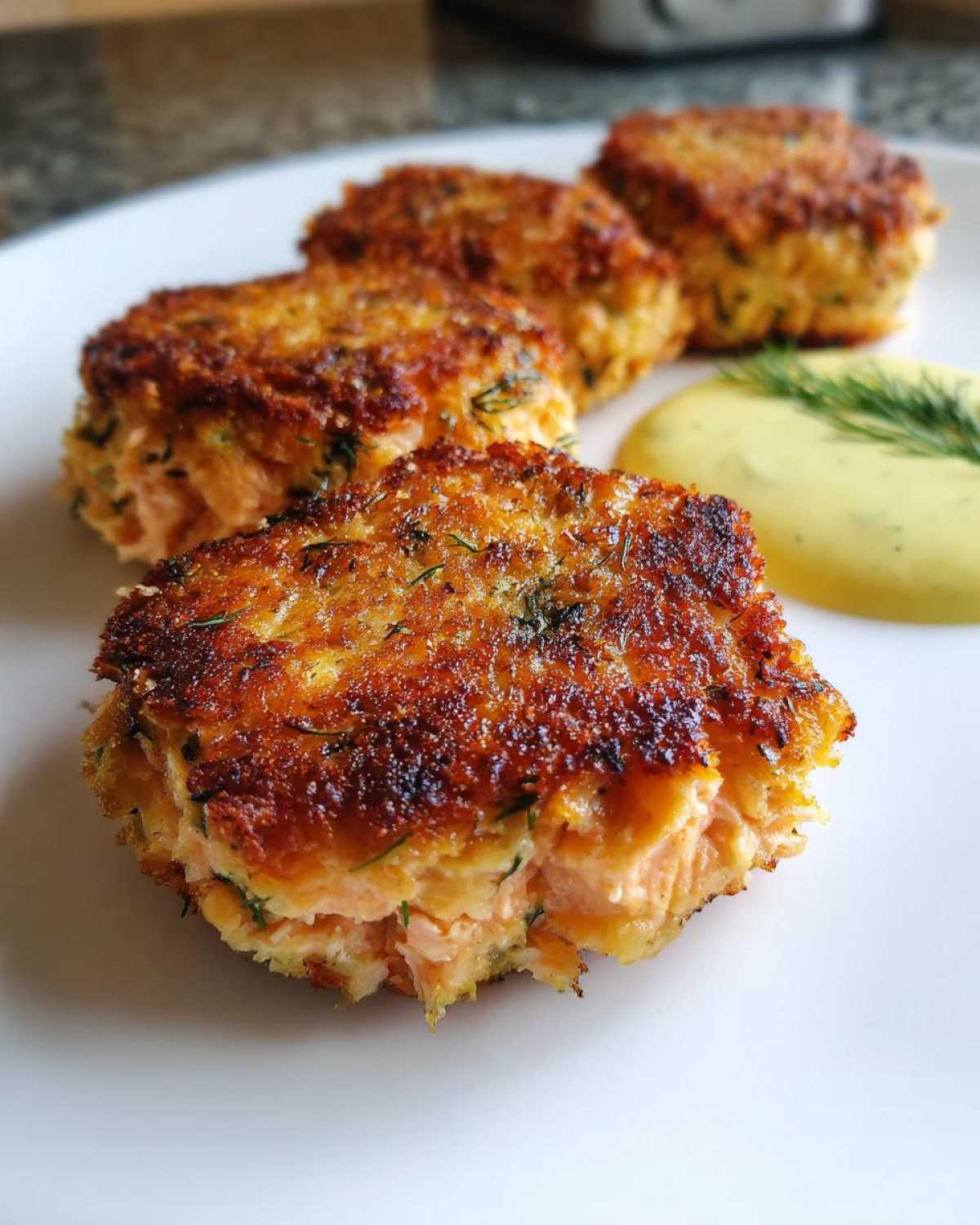 A close-up of a golden-brown, crispy salmon cake showing the flaky interior, served with a dollop of yellow sauce.